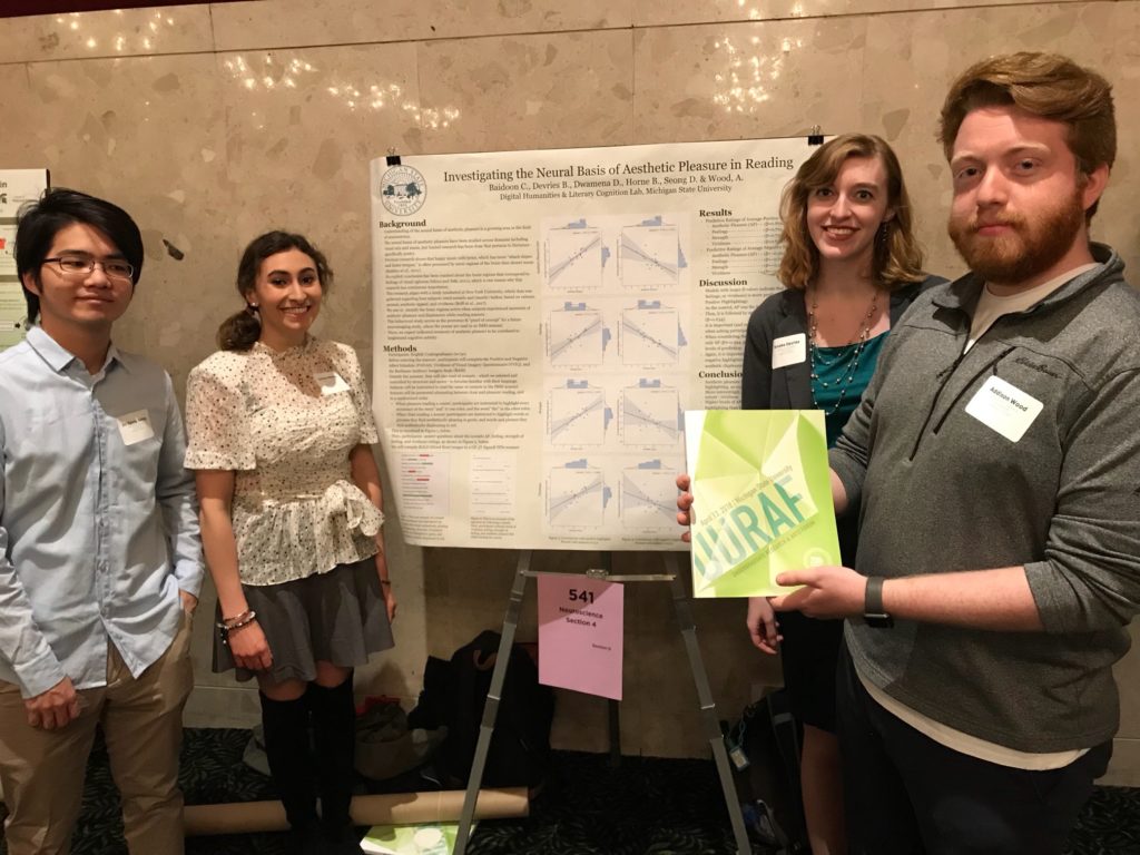 Four lab members stand in front of their research poster smiling. 
