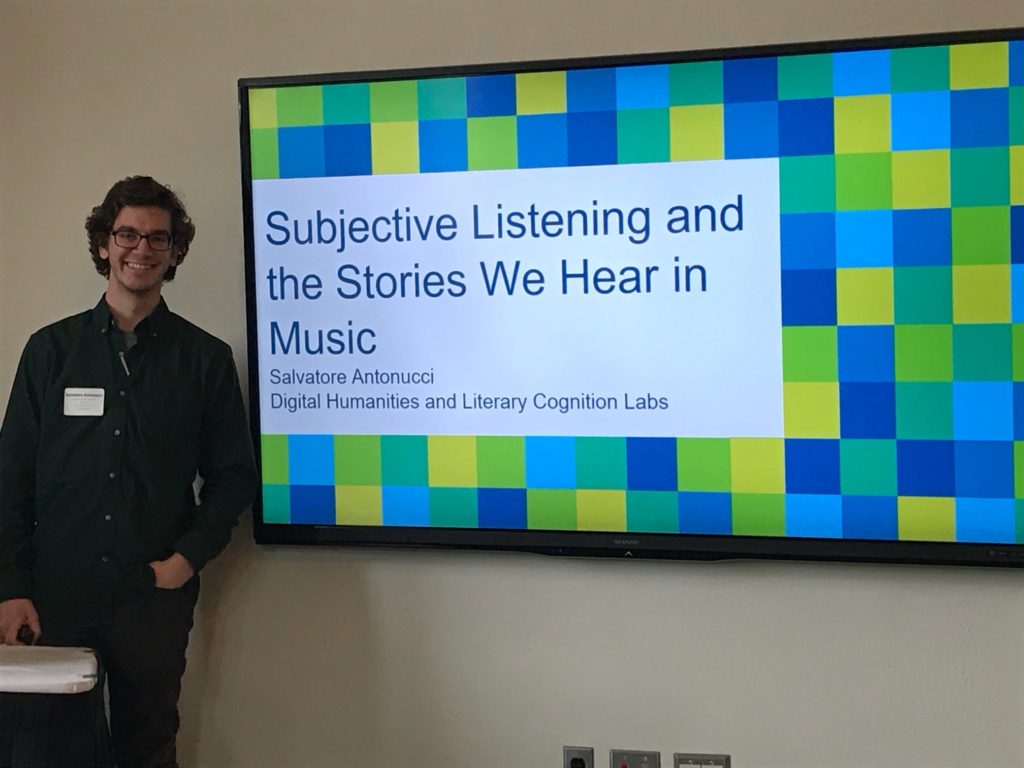 A lab member stands in front of a large screen that reads, "Subjective Listening and the Stories We Hear in Music."